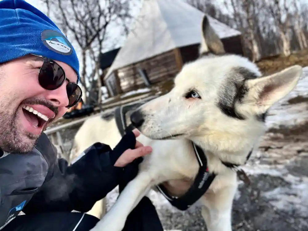 Man in blue hat and sunglasses with white sled dog
