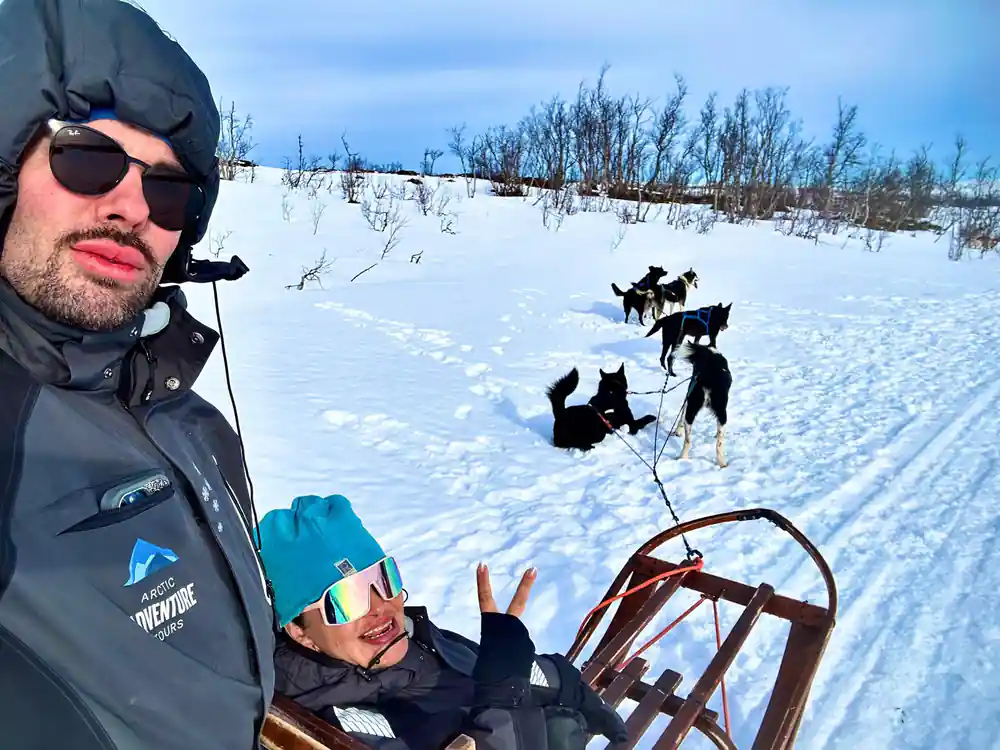 Man on sled with four black sled dogs on snowy landscape