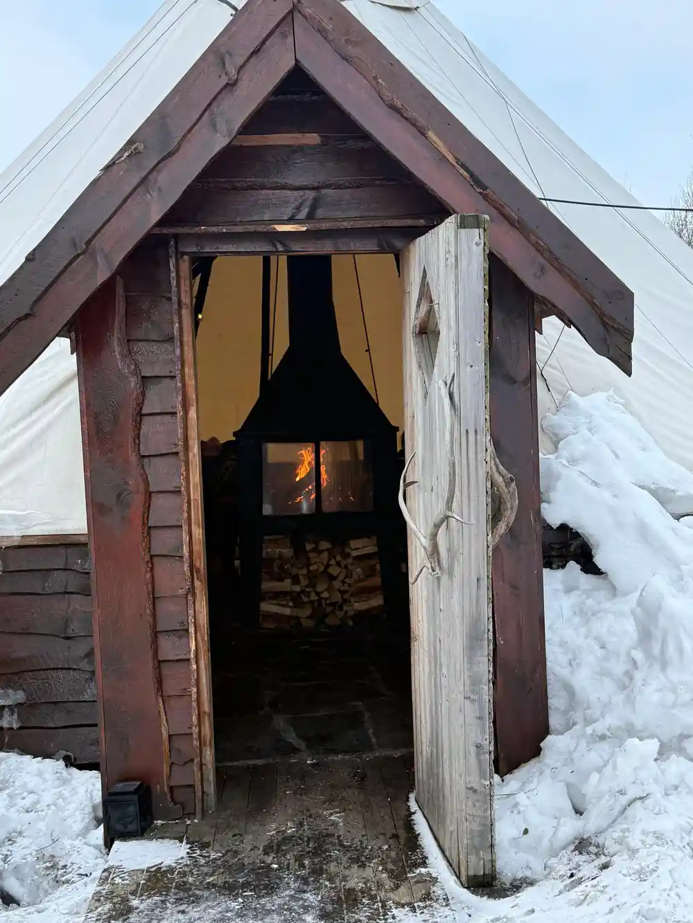 Small wooden cabin with open door and stove inside
