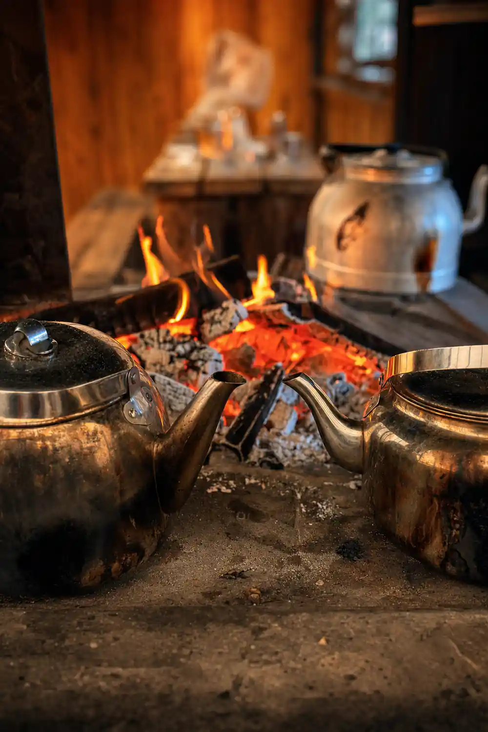 Teapots heating on open fire with flames and coals
